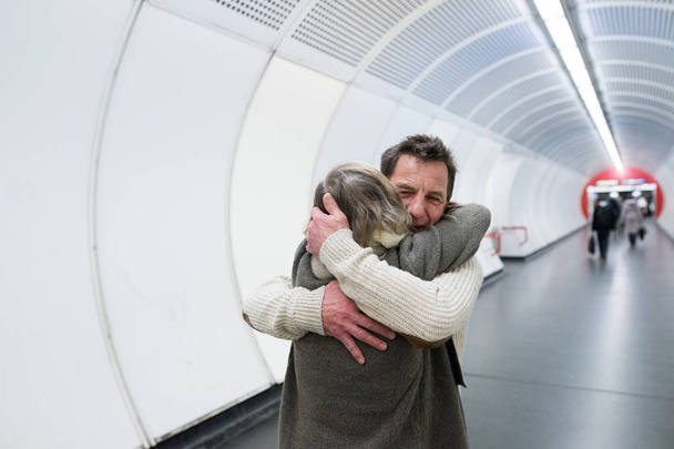 Senior couple in winter clothes in hallway of subway hugging - Photo, Image