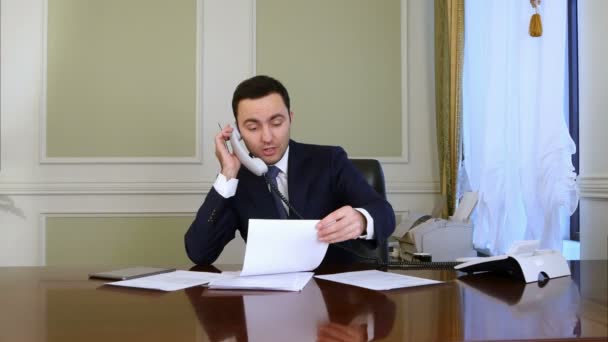 Young confident successful businessman working in modern office analyzing business by phone conversation - Záběry, video
