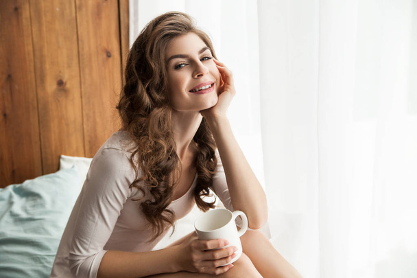 Smiling woman with cup at the window - Photo, image