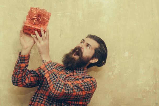 Surprised bearded man holding red gift box with bow - Фото, изображение