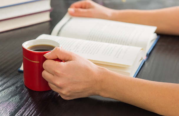 Woman hands holding open book with pile of closed books and cup of coffee home.. - Foto, Imagen