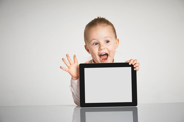 Cute little and smiling girl plays with a tablet - Fotografie, Obrázek