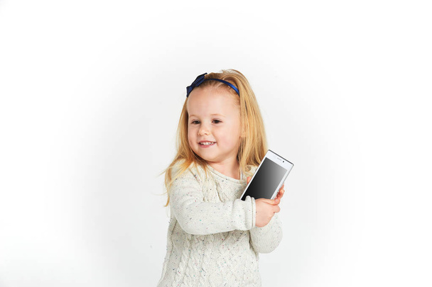 Cute little girl smiling and uses a smartphone, phone. - Φωτογραφία, εικόνα