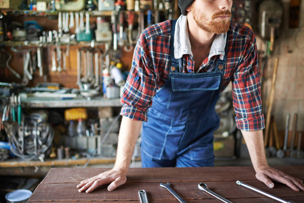 Mann stützt sich mit Schraubenschlüssel auf Tisch  - Foto, Bild