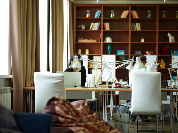 暖かい茶色の色調の内装とモダンな事務室の背の高い本棚に対してランプ木製ワーキング デスク - 写真・画像