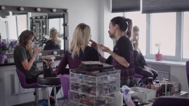 Best friends together came to a beauty salon to make a beautiful hair and makeup before a cool party. Girl sits on a high chair with a smartphone and waiting when specialist will be available. - Footage, Video