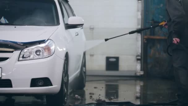 Travailleur en service automobile lave une voiture dans la mousse par des tuyaux d'eau
 - Séquence, vidéo