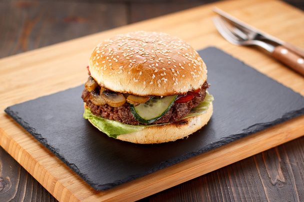 Big burger on a stone plate and wooden background. - Φωτογραφία, εικόνα