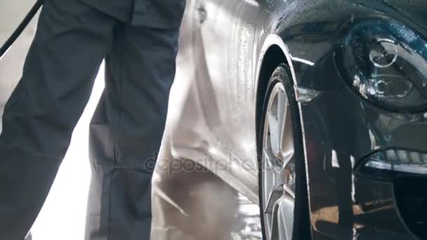 Travailleur dans le garage service automobile lave une voiture dans la mousse par des tuyaux d'eau - vue rapprochée
 - Séquence, vidéo
