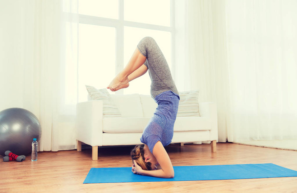 woman making yoga in headstand pose on mat - Фото, изображение