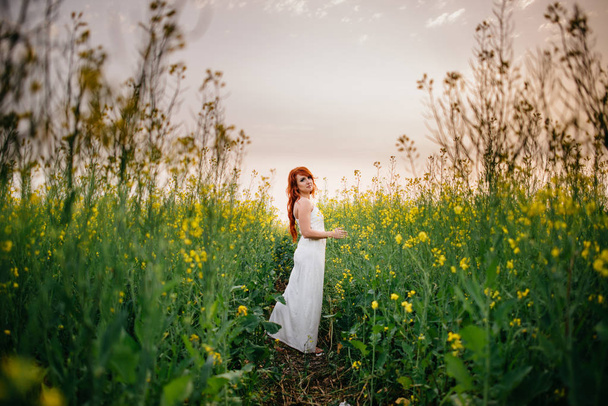 Young red-haired woman in a rapeseed field - Фото, зображення