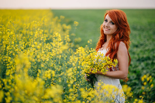 Young red-haired woman in a rapeseed field - Foto, Imagem