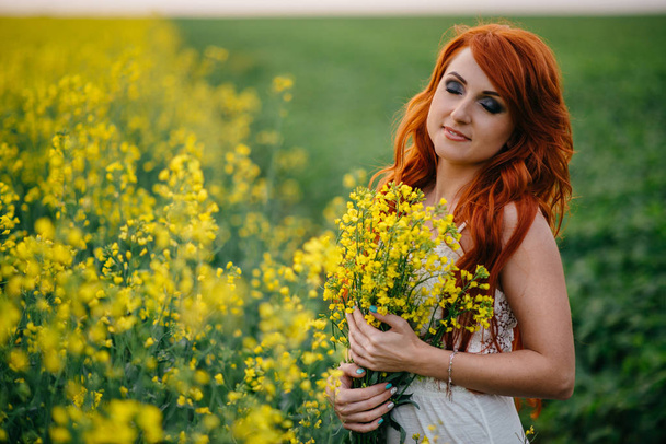 Young red-haired woman in a rapeseed field - Φωτογραφία, εικόνα