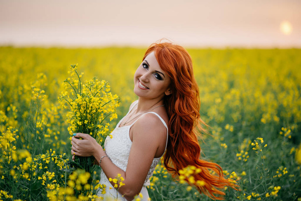 Young red-haired woman in a rapeseed field - Foto, Imagem