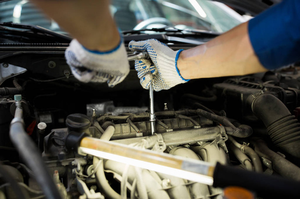 Mechaniker mit Schraubenschlüssel repariert Auto in Werkstatt - Foto, Bild