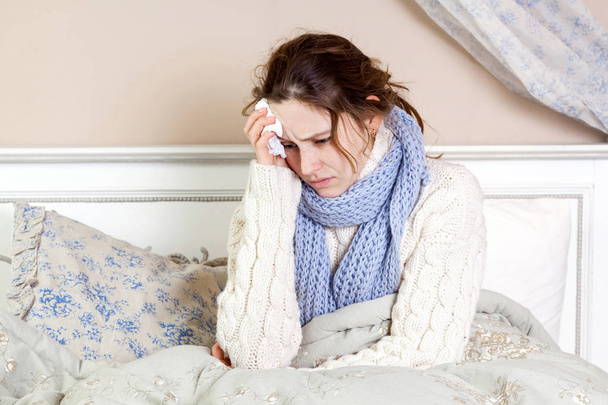 Flu or cold. Closeup top view image of frustrated young woman with blue scarf and suffering from terrible headache while lying in bed. - Foto, Imagem