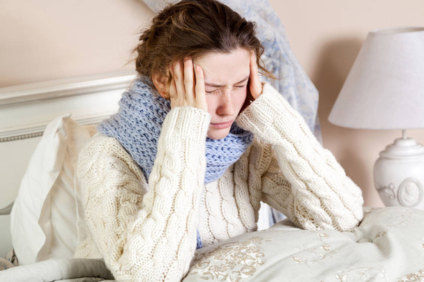 Flu or cold. Closeup top view image of frustrated young woman with blue scarf and suffering from terrible headache while lying in bed. - Fotó, kép