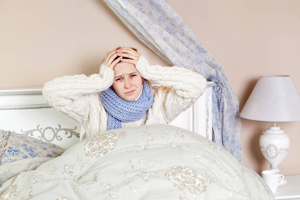 Flu or cold. Closeup top view image of frustrated young woman with blue scarf and suffering from terrible headache while lying in bed. - Фото, зображення