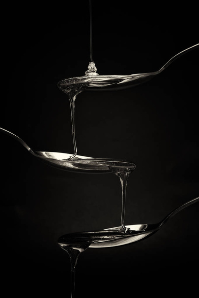 Miele versando da cucchiaio su uno sfondo scuro
 - Foto, immagini