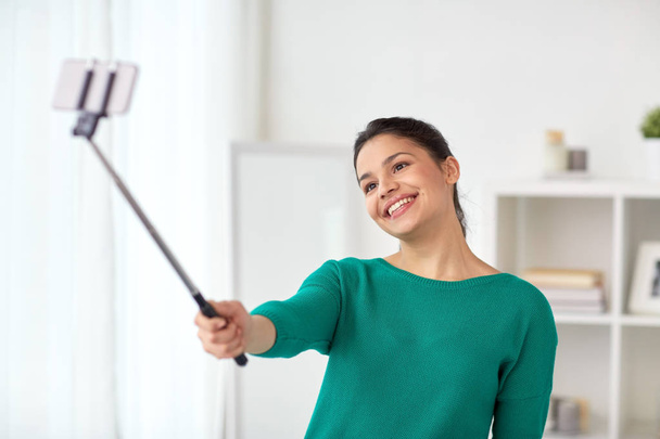 woman taking selfie by smartphone monopod at home - Фото, изображение