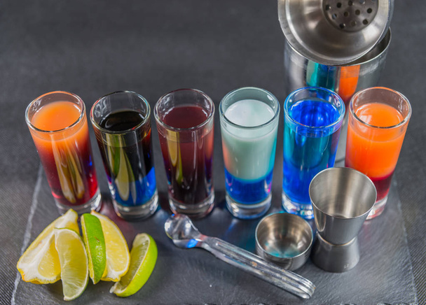 six different colored shot drinks, lined up on a black stone pla - Photo, Image
