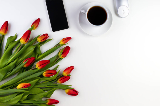 Mesa de escritorio de oficina con teléfono móvil, cuaderno de papel, taza de café y hermoso ramo de flores frescas tulipanes
 - Foto, Imagen
