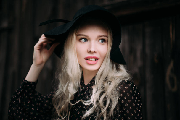 Krásná atraktivní a elegantní dívka, která nosí černý klobouk postavení pózuje v městě. Nahé líčení, denní účes a velké módní glamour venkovském stylu. Retušované fotografie - Fotografie, Obrázek