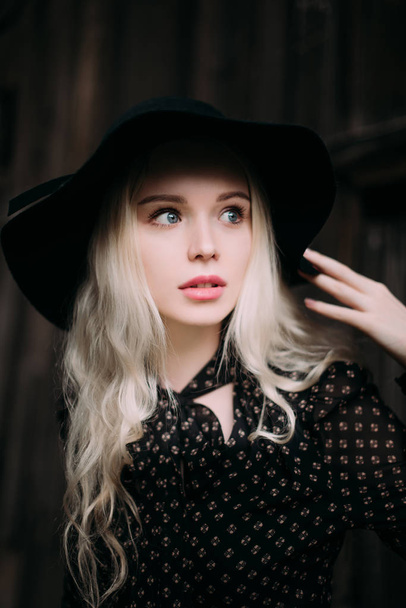 Beautiful attractive and stylish girl wearing black hat standing posing in city. Nude makeup, best daily hairstyle and great fashion glamour country style. Retouched photo - Photo, image