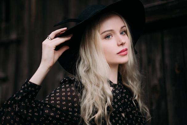 Beautiful attractive and stylish girl wearing black hat standing posing in city. Nude makeup, best daily hairstyle and great fashion glamour country style. Retouched photo - Photo, Image