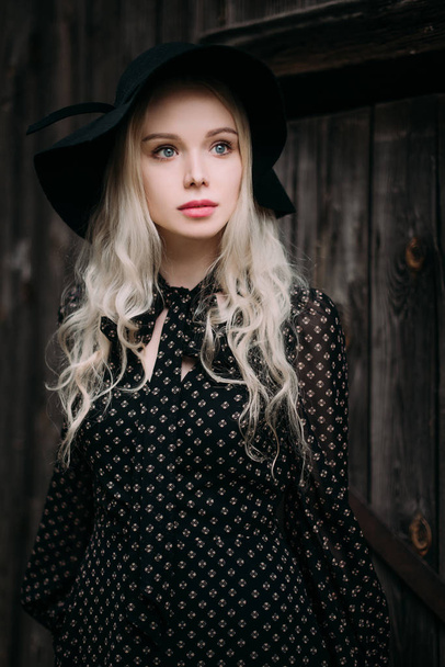 Όμορφη ελκυστική και μοντέρνα κοπέλα φορώντας μαύρο καπέλο στέκεται ποζάρουν στην πόλη. Nude μακιγιάζ, καλύτερο καθημερινό χτένισμα και μεγάλη Μόδα γοητεία εξοχικό στιλ. Retouched φωτογραφία - Φωτογραφία, εικόνα