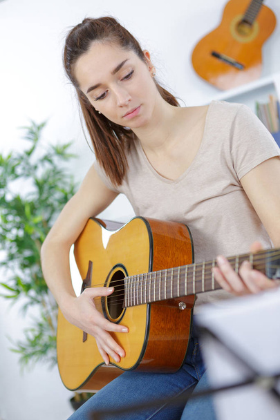 beautiful girl sitting on the sofa and playing guitar - Foto, Imagem