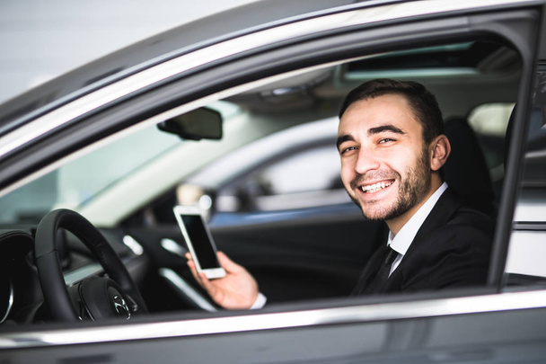 Επιχειρηματία στο αυτοκίνητο χρήση smartphone και χαμόγελο στην κάμερα - Φωτογραφία, εικόνα