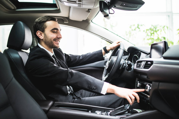 close up of young man in suit driving car and switching some button on panel of car - Fotoğraf, Görsel