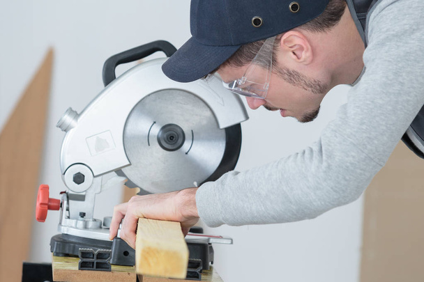carpenter cutting plank of wood with circular disc saw - Foto, afbeelding