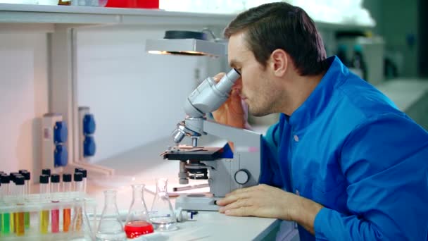 Mężczyzna naukowcem robi badania mikroskopem. Człowiek uczony szuka mikroskopu - Materiał filmowy, wideo