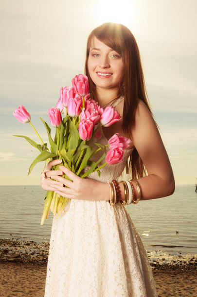 Portrait of woman holding pink flowers on beach - Zdjęcie, obraz