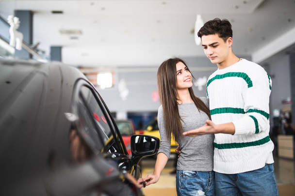 Красива молода пара стоїть в дилерському центрі, вибираючи машину, щоб купити
 - Фото, зображення