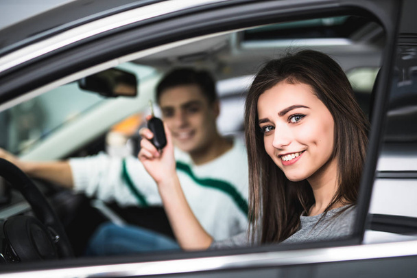 Beautiful young couple sitting at the front seats of their new car while woman showing keys and smiling - Foto, immagini