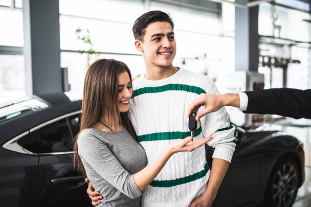 Щаслива пара дивиться на руку продавця, отримуючи ключі від машини
 - Фото, зображення