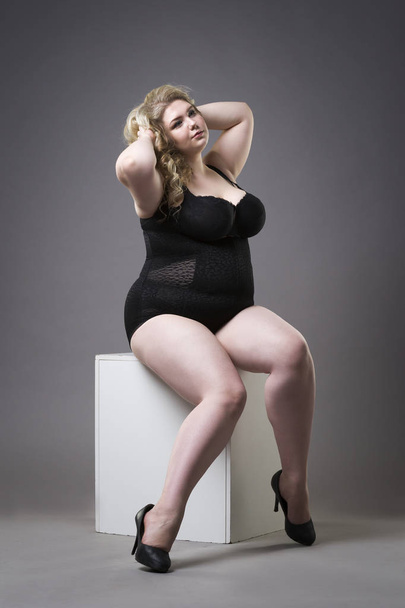 Young beautiful blonde plus size model in shapewear, xxl woman in slimming underwear on gray studio background - 写真・画像