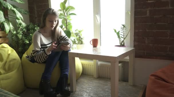 Teenager girl sitting at the table and using tablet - Felvétel, videó