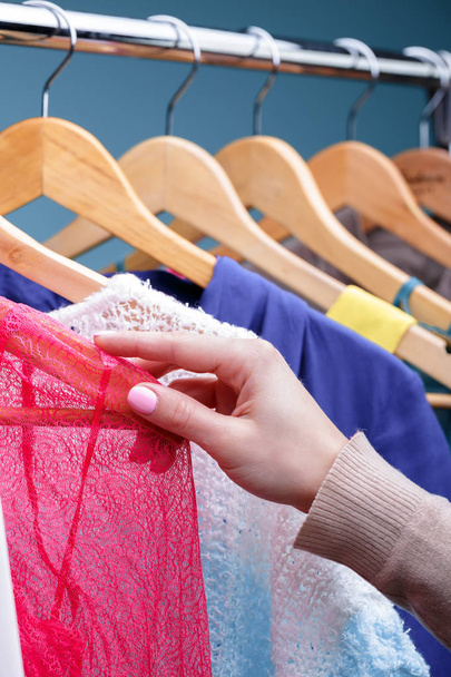 vrouwelijke hand selecteert kleurrijke kleding op houten hangers op rek in - Foto, afbeelding