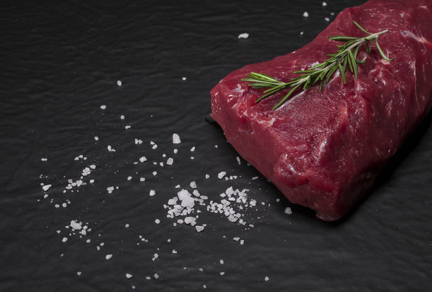 Raw beef steak on a cutting board with rosemary and spices. - Foto, Imagen