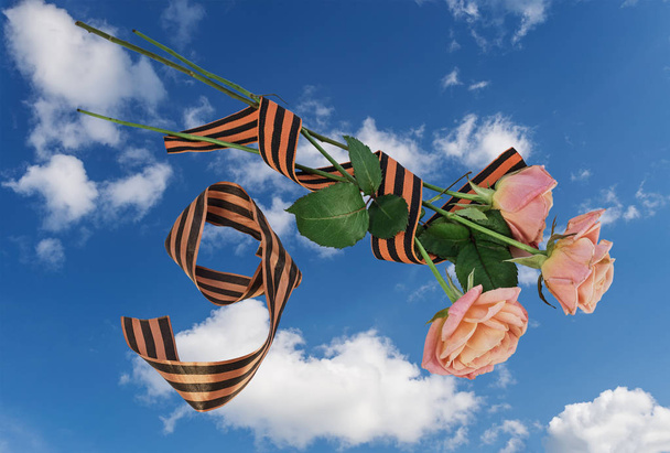 Tre rose e un nastro di San Giorgio, un bouquet per il Giorno della Vittoria contro un cielo blu con le nuvole
. - Foto, immagini