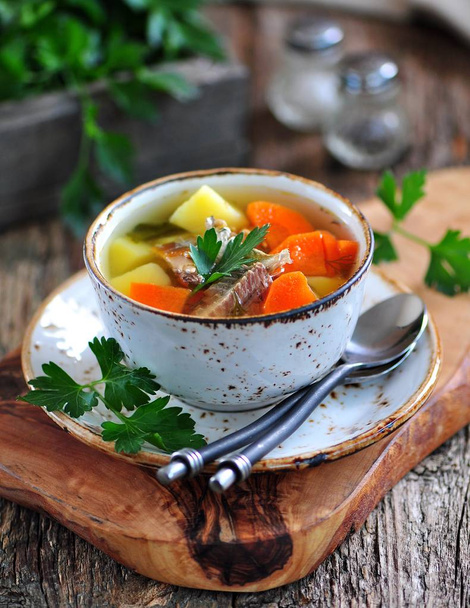 Fish soup with potatoes, carrots and parsley on the old wooden background. - Photo, Image