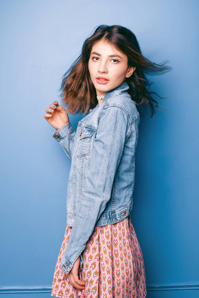 Beautiful positive girl in a jeans jacket on a blue background smiling and posing - Foto, immagini