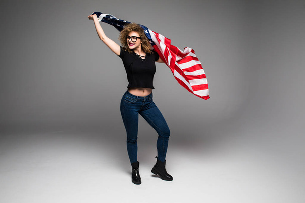 Wesoła, młoda kobieta w ubranie jest fala flaga amerykańska i uśmiecha się na szarym tle - Zdjęcie, obraz