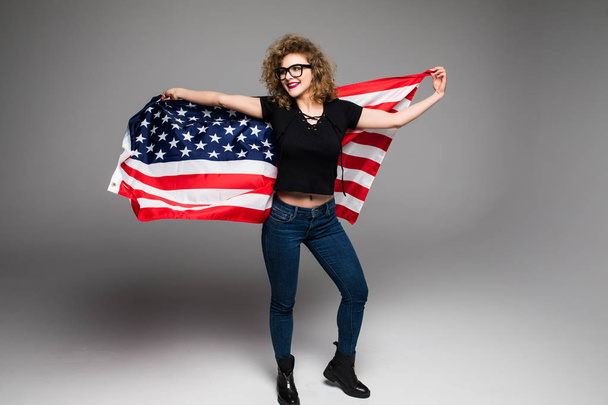 Веселий молоду жінку в повсякденний одяг є хвиля американським прапором і посміхається на сірий фон - Фото, зображення