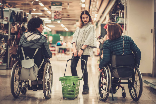 Jeune fille aidant deux femmes handicapées en fauteuil roulant dans un grand magasin
 - Photo, image