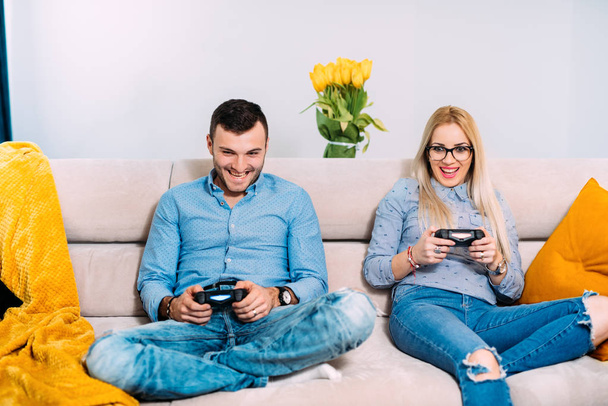 happy couple playing digital video games with joystick controller while sitting on sofa or couch. modern details of digital technology - Foto, immagini